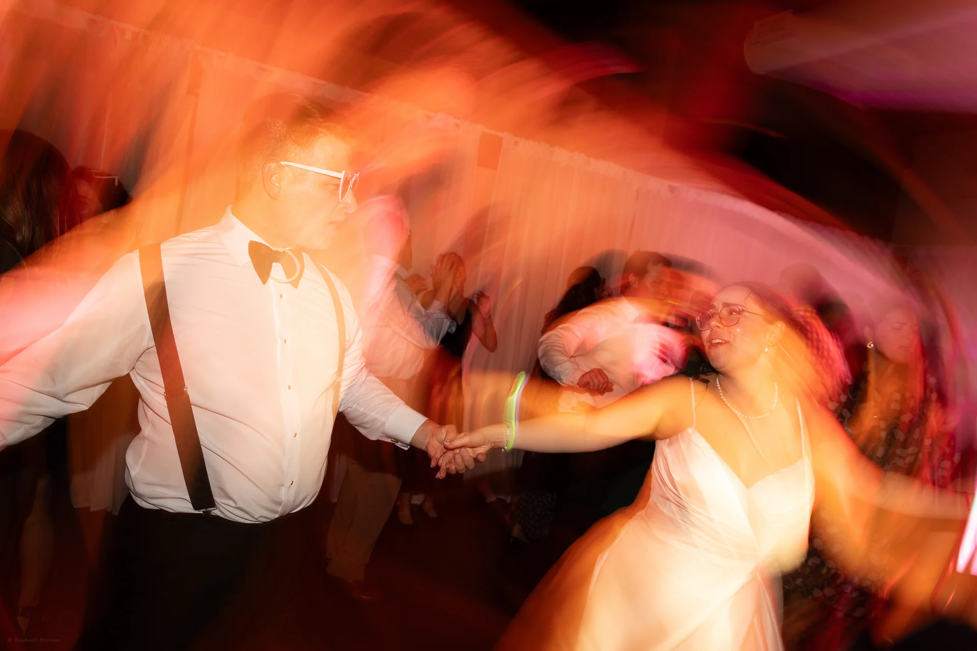 Un couple danse sous une lumière orangée, avec un flou de mouvement expressif.