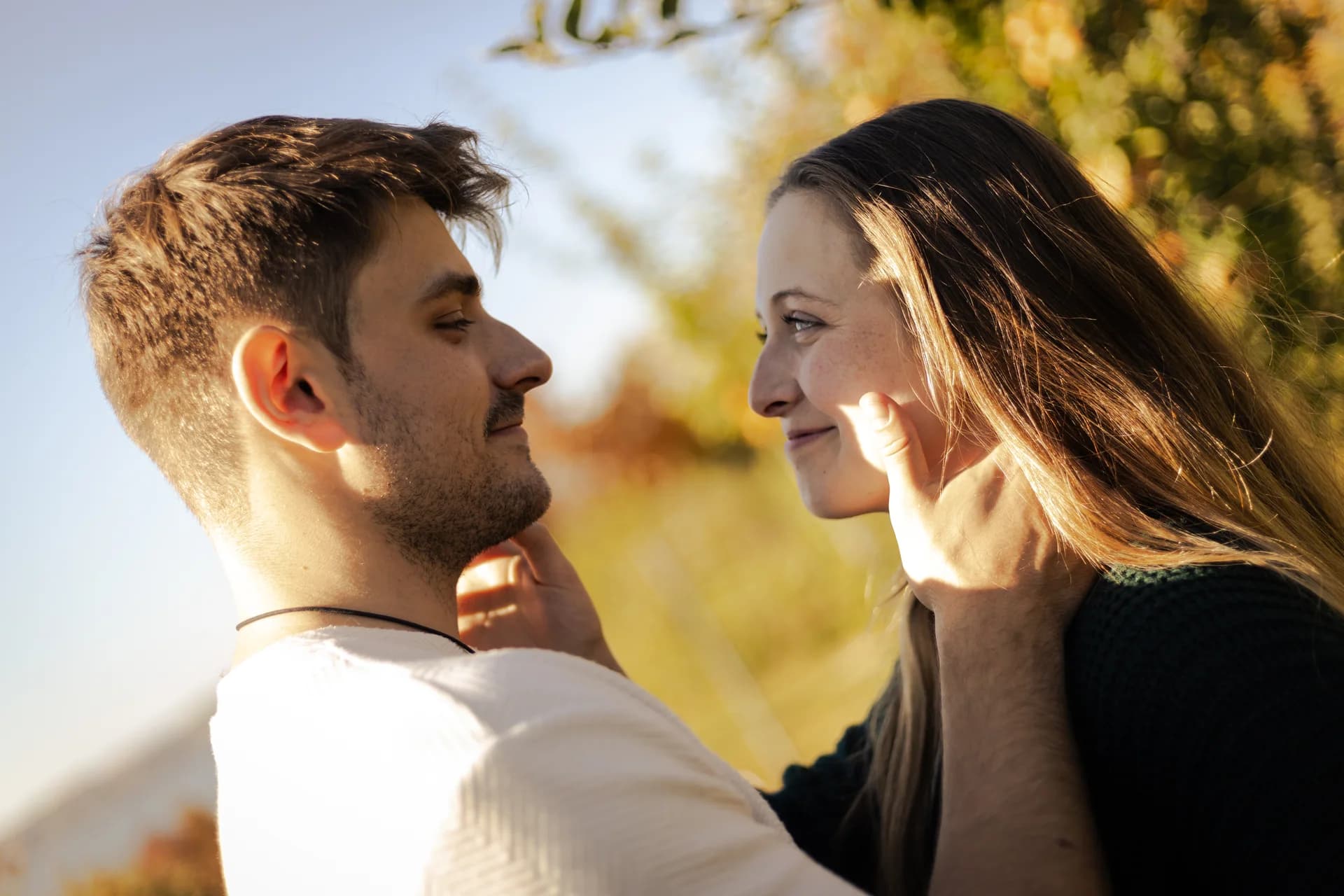 A couple looks at each other and smiles in sunlight.