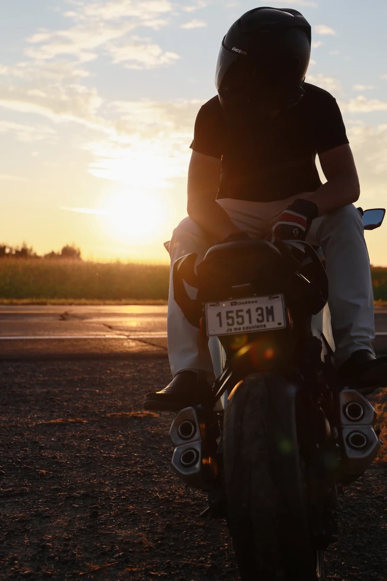 Une personne assise sur une moto, en silhouette au coucher du soleil.